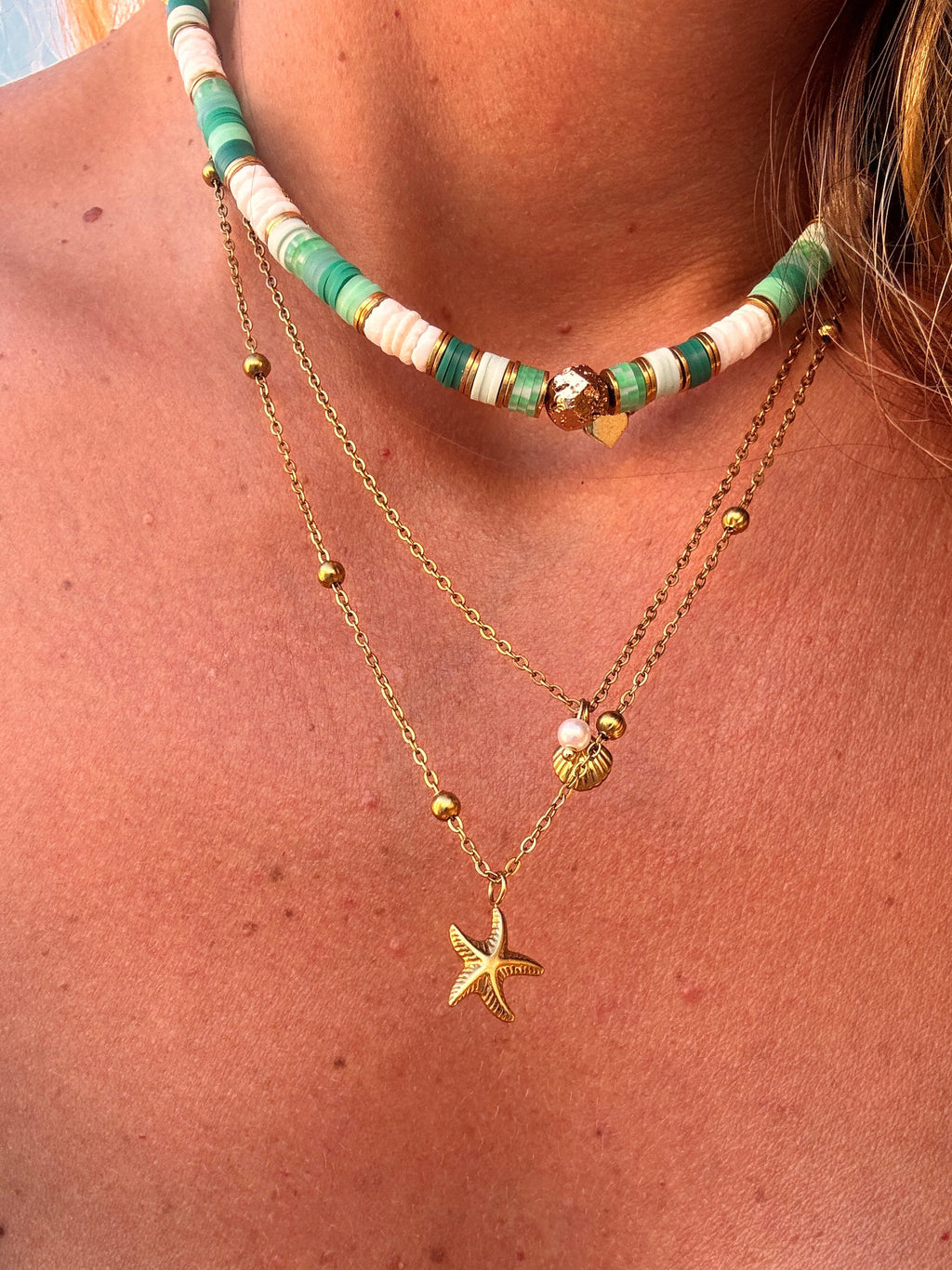 Collier Palma en perles heishi vertes et rose poudré porté près du cou, avec chaînes dorées en layering
