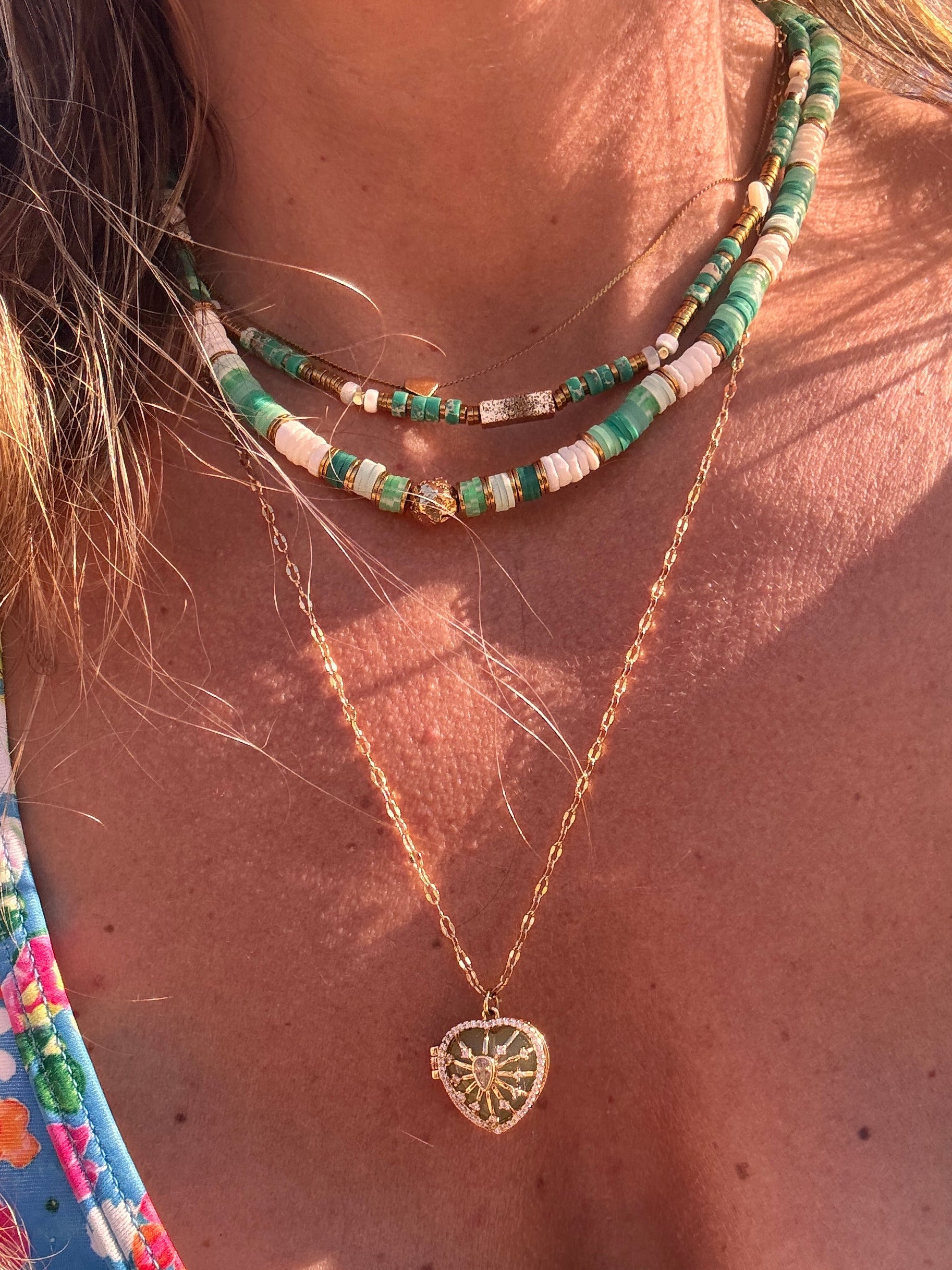 Détail du collier Palma : perle dorée martelée et pampille cœur entre perles heishi vertes